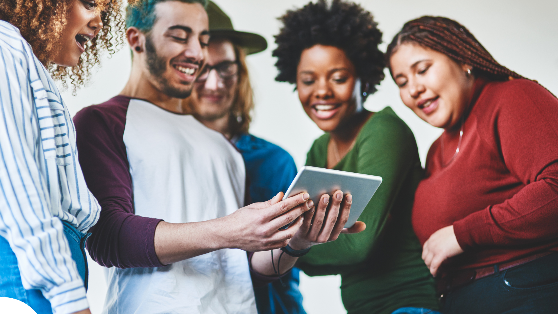 A group of five people stand closely together, smiling and focused on a tablet device held by one of them. The group is diverse, with different hairstyles, clothing styles, and skin tones, reflecting inclusivity. Un groupe de cinq personnes se tient rapproché, souriant et concentré sur une tablette tenue par l’une d’elles. Le groupe est diversifié, avec des styles de cheveux, de vêtements et de teints variés, reflétant l’inclusivité.